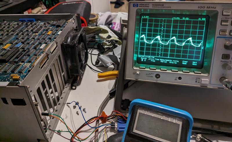 Photo of the computer and an analog oscilloscope "HP 54600B 100 MHz" showing the same wave zoomed in. A multimeter can be seen at the bottom of the image, alongside with many wires plugged to different things.